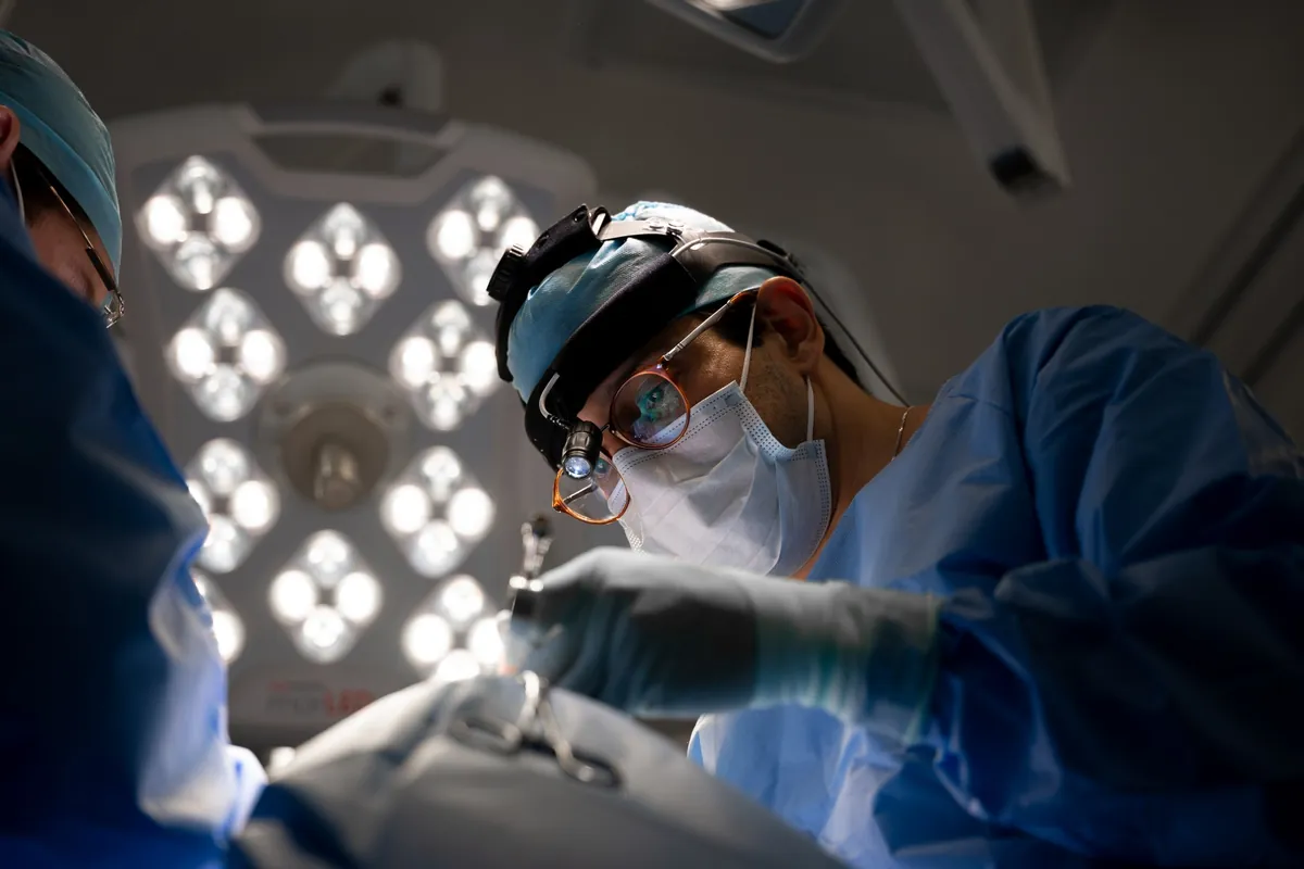 Dr. Leandro Ventura operando, com lupa e luz de cabeça, sob o foco cirúrgico