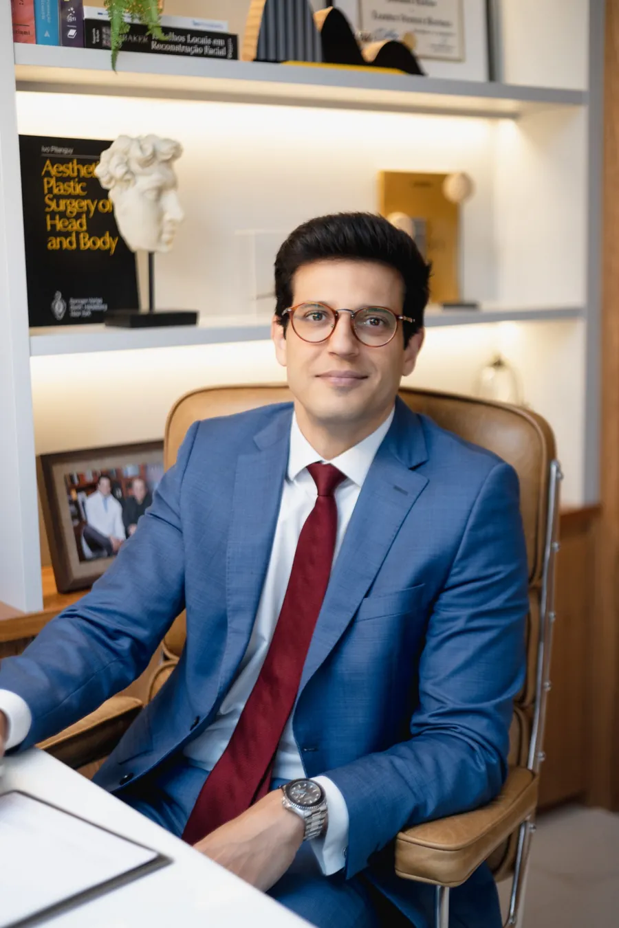 Dr. Leandro Ventura de terno azul, sentado no consultório